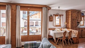 A cozy living room with a sofa, a dining table with chairs, wooden cabinets, and large windows with curtains. - Chesa Mezzaun by Interhome (Zuoz)