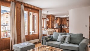 A cozy living room with a sofa, ottoman, and foosball table. There is a dining area with a table and chairs, and wooden cabinets in the kitchen. - Chesa Mezzaun by Interhome (Zuoz)