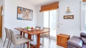 A dining area with a wooden table and chairs, a painting on the wall, and a window with a bamboo blind.