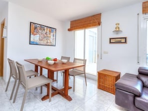 A dining area with a wooden table and chairs, a painting on the wall, and a window with a bamboo blind.
