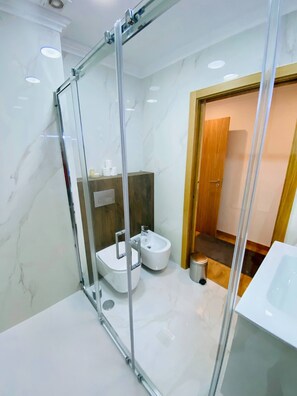 Ein modernes Badezimmer mit Glastrennwand, einem Bidet, einer Toilette und einem Waschbecken.