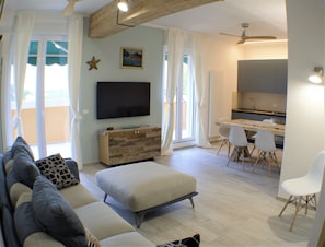 Een moderne woonkamer met een bank, voetenbankje en een flatscreen televisie aan de muur.