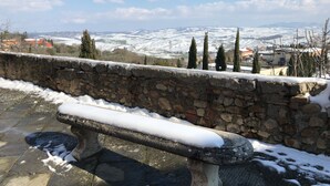 A stone bench with snow on it, overlooking a snow-covered landscape with buildings and trees.