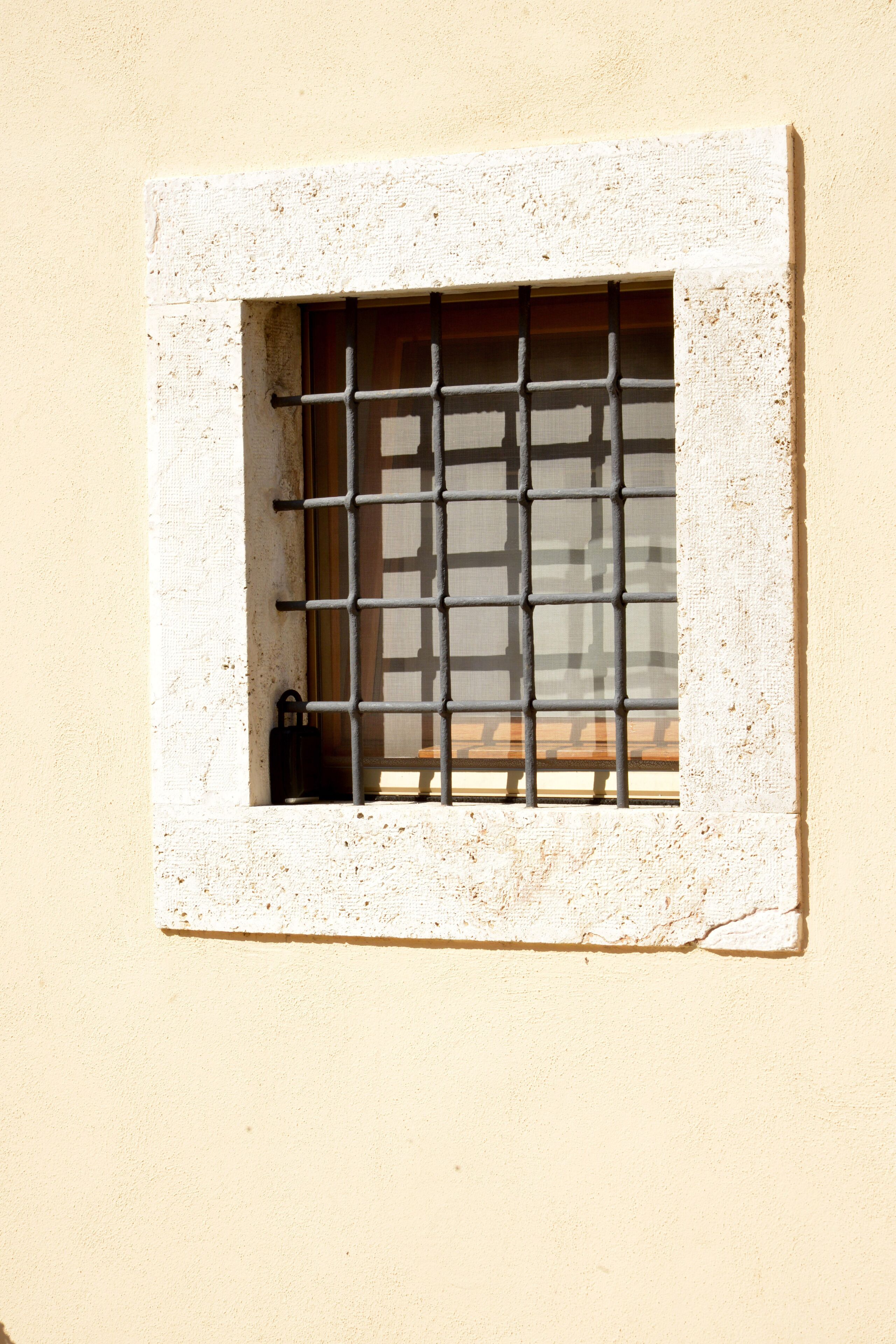 Una ventana con barrotes de metal, un objeto pequeño en el alféizar y una pared con textura.