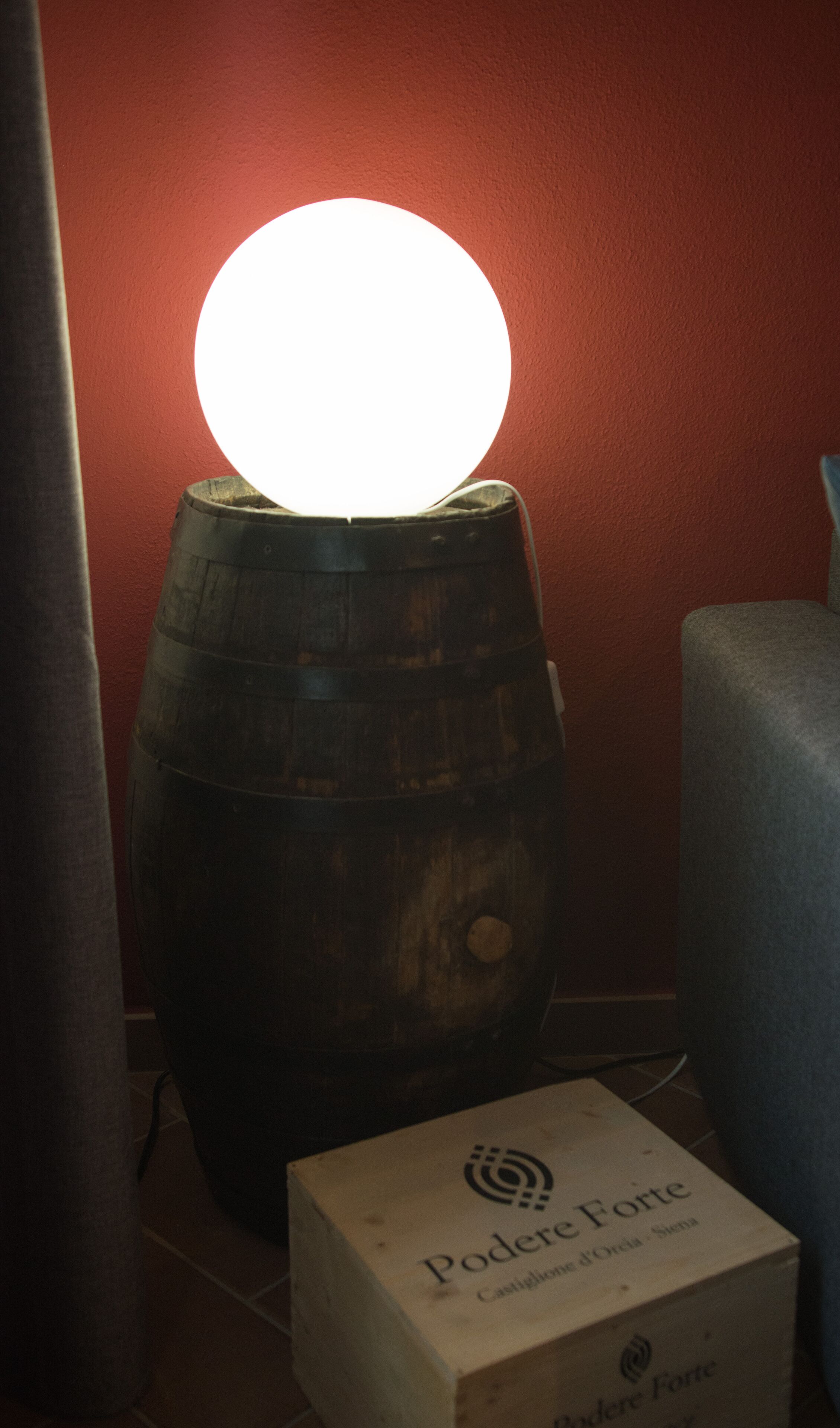 A wooden barrel with a glowing light on top, placed against a red wall.