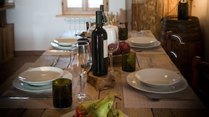A wooden dining table set with plates, glasses, and a bottle of wine, with a window and wooden wall in the background.