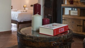 A rustic room with a wooden barrel table, a lamp, a book, and a bed in the background.