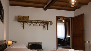 A bedroom with a wooden ceiling, a bed with white linens, a bedside table with a lamp, and a wooden shelf above the bed.