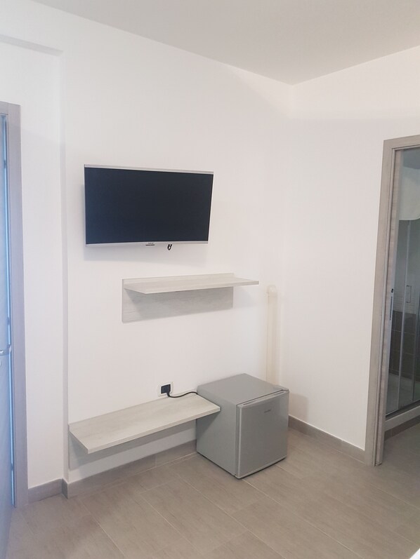 Una habitación moderna con una televisión de pantalla plana montada, estanterías empotradas y un refrigerador compacto.