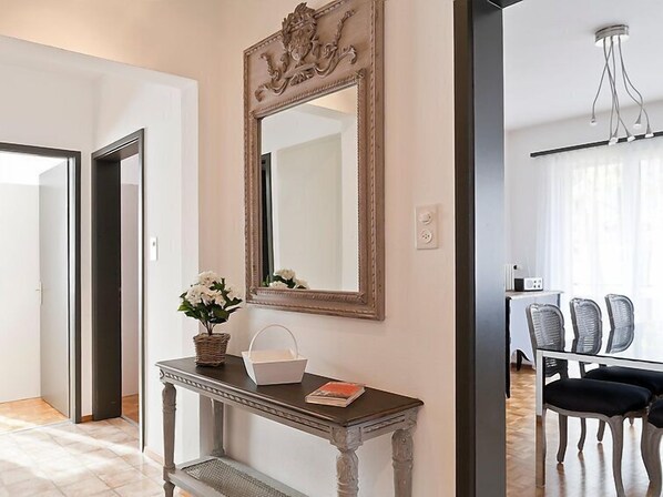 A hallway with a decorative mirror, a console table with a vase and a basket, and a dining area with chairs and a table.