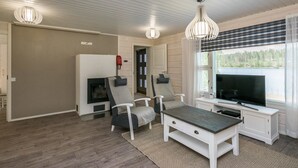 Una sala de estar con chimenea, dos sillones, una mesa de centro, un televisor y una ventana con persianas.