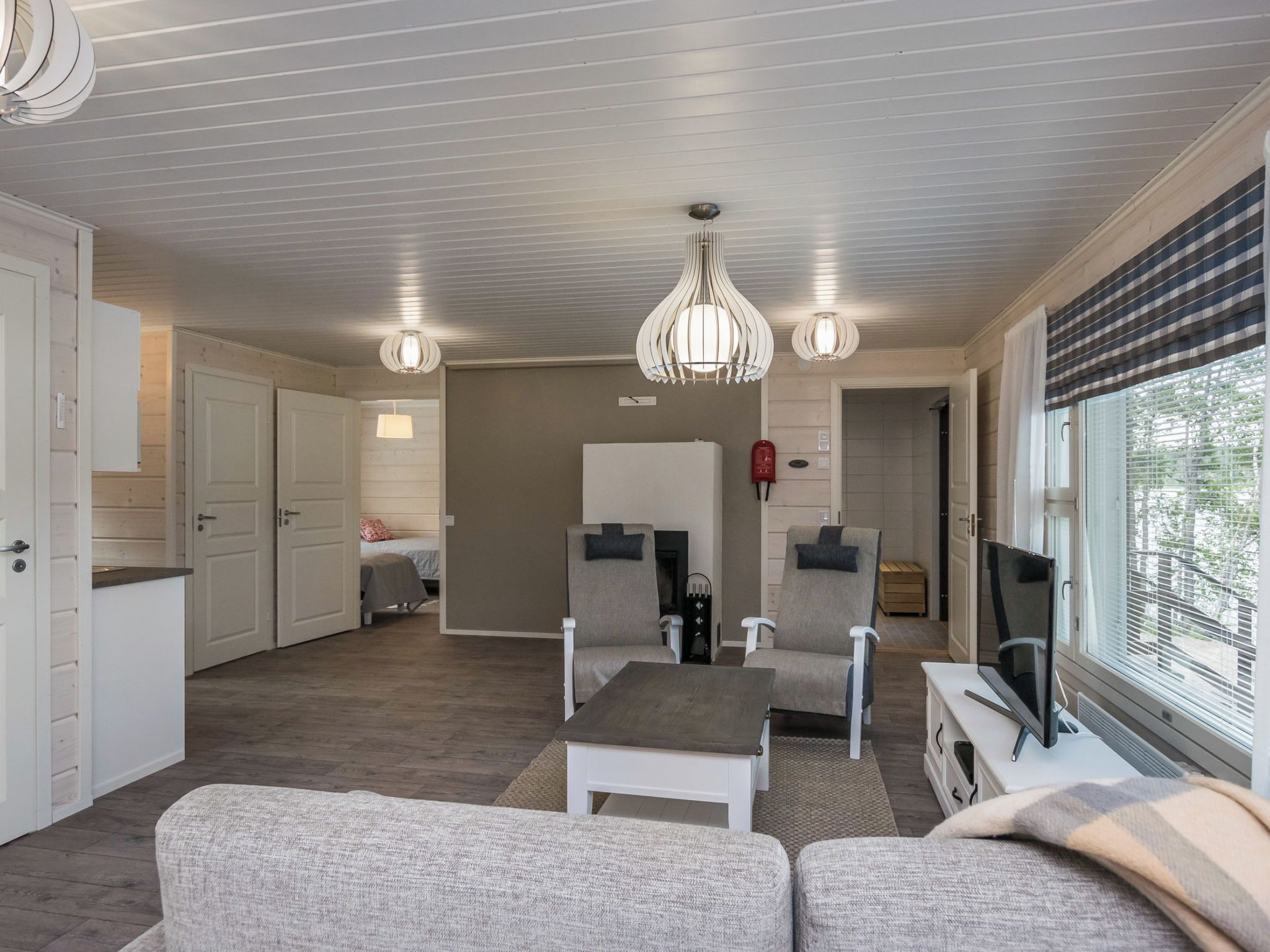 Amplia sala de estar con un conjunto de sofás, una mesa de centro y dos sillones. Hay un televisor sobre un mueble bajo y una ventana con persianas.