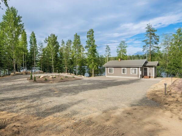 A two-story house with a gravel driveway, surrounded by trees and a body of water.