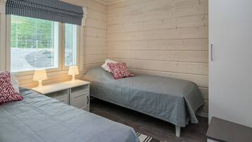 A room with two beds, a window with blinds, a lamp, and a wardrobe.