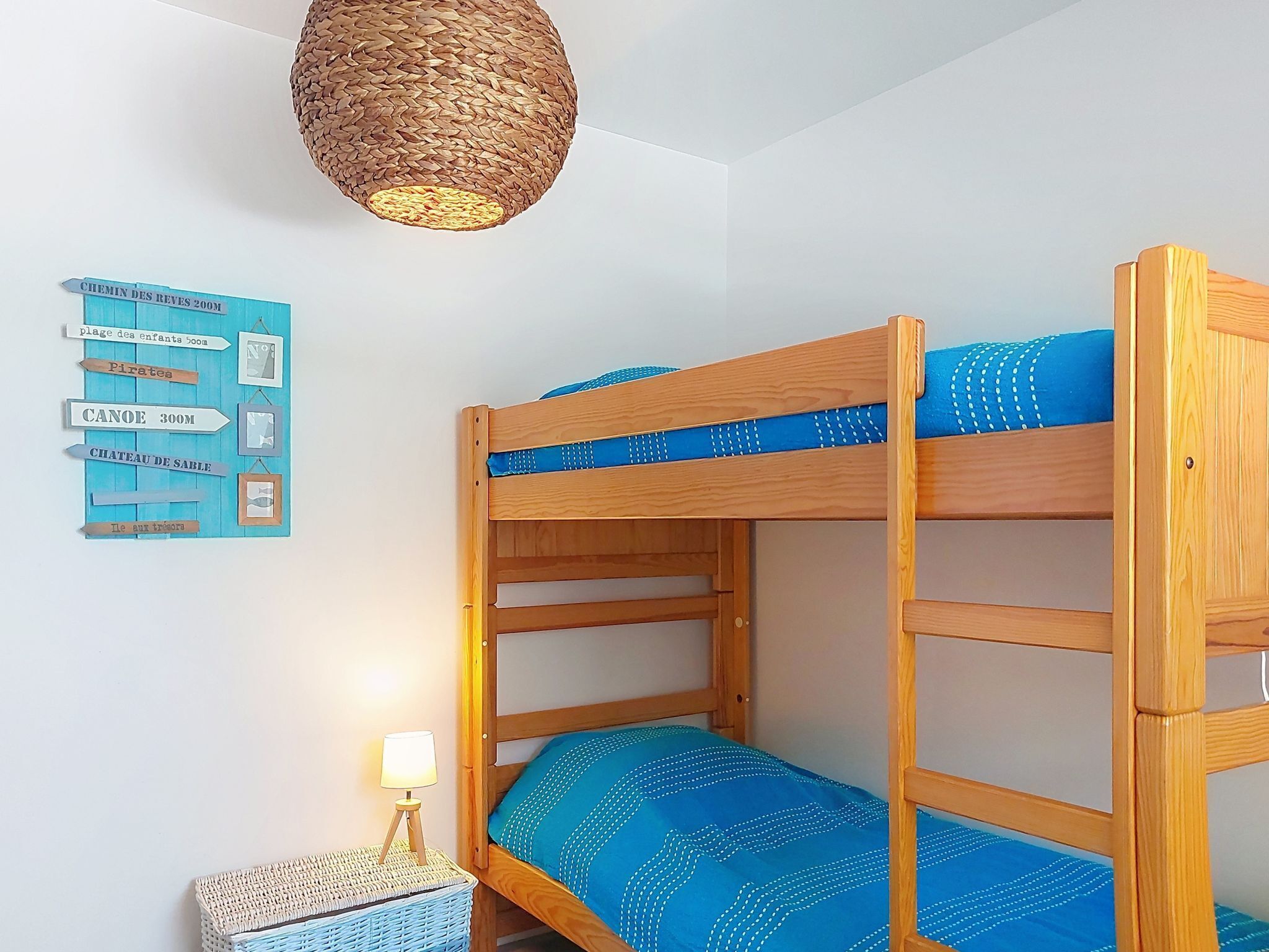 A bunk bed room with a woven light fixture, a wall map, and a small table with a lamp.