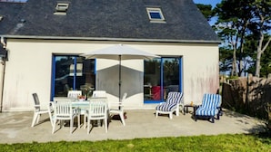 A house with a patio area featuring a table and chairs, a large umbrella, and a sliding glass door leading to an interior space. - La Brise by Interhome (Quiberon)