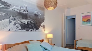 A bedroom with a bed, a hanging light fixture, a wall-mounted lamp, a framed picture, and a door leading to another room. - La Brise by Interhome (Quiberon)
