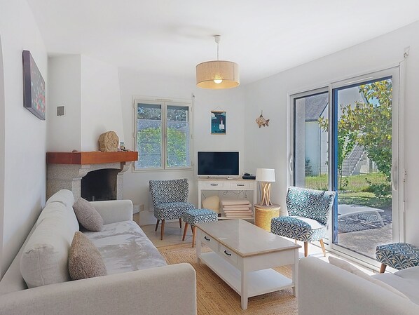 A living room with a fireplace, sofa, TV, and a view of greenery outside.