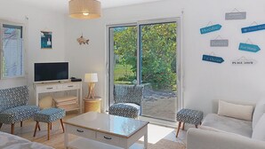 A modern living room with a TV, sofa, and chairs, a dining table, and a large sliding glass door leading to a garden. - La Brise by Interhome (Quiberon)