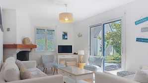 A modern living room with a fireplace, a TV, and a large sliding glass door to the outdoors. - La Brise by Interhome (Quiberon)