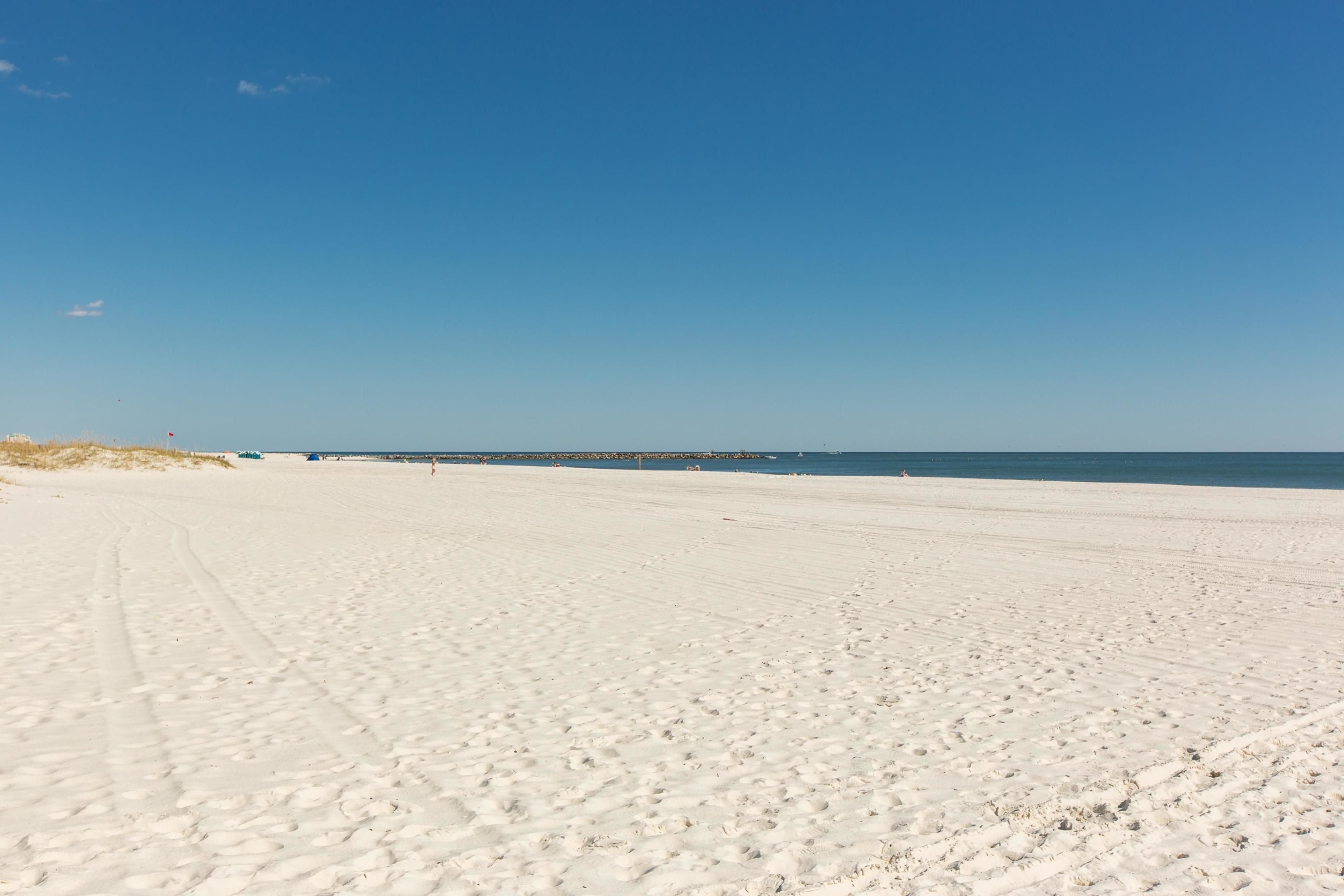 A wide sandy beach with footprints and a clear blue sky.