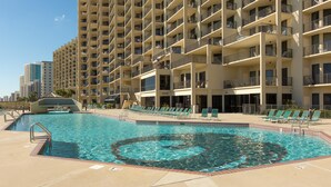 Une piscine de forme circulaire, entourée de chaises longues et d’un immeuble de grande hauteur doté de balcons.