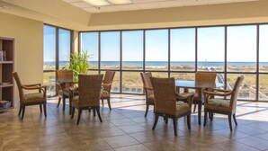 Une pièce spacieuse avec de grandes fenêtres donnant sur la plage. On y trouve des chaises en osier et une table en verre.