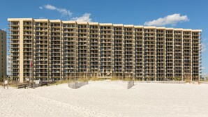 Un hôtel de grande hauteur, avec de nombreux étages, une plage de sable en premier plan et un ciel bleu dégagé.