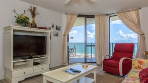 Un salon avec un téléviseur, un fauteuil rouge, un canapé et un balcon donnant sur la mer.