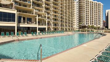 A hotel with a large pool area, multiple balconies, and a clear blue sky.