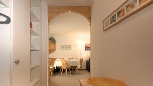 A hallway with a wooden door, a dining area with a table and chairs, and a wooden bench with a glass bowl. - Chesa Flora 53 by Interhome (St. Moritz)