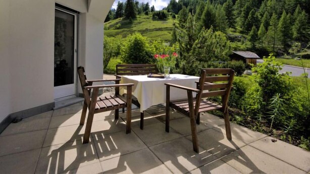 A patio with a table and chairs, overlooking a lush green landscape and a mountain. - Chesa Flora 53 by Interhome (St. Moritz)