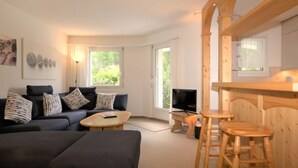 A modern living room with a sofa, coffee table, and wooden bar stools. - Chesa Flora 53 by Interhome (St. Moritz)