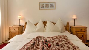 A bedroom with a bed, two bedside tables, a nightstand, a framed picture on the wall, and a window with curtains. - Chesa Flora 53 by Interhome (St. Moritz)