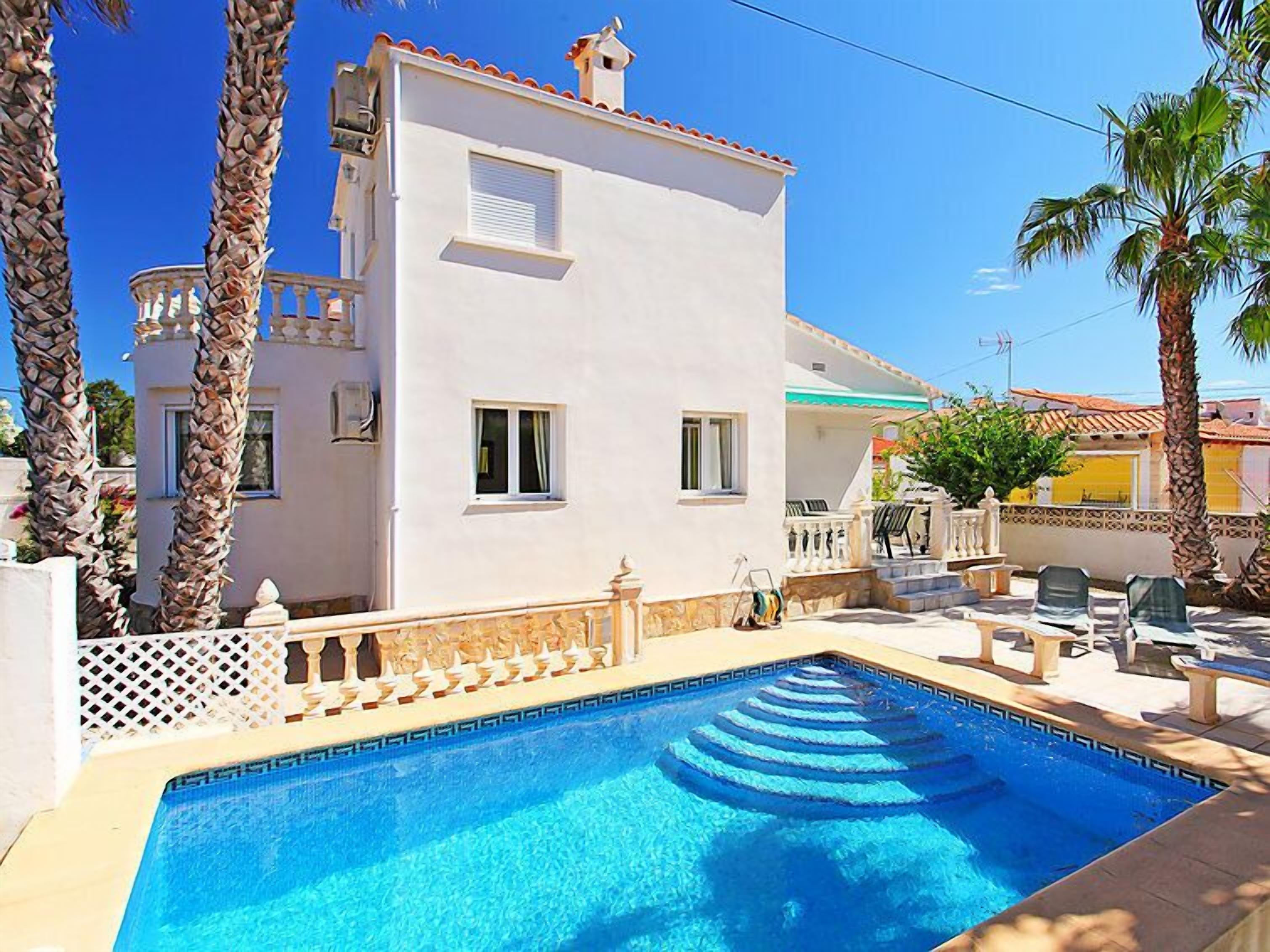A white villa with a swimming pool, palm trees, and outdoor furniture.