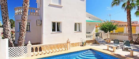 Eine weiße Villa mit Swimmingpool, Palmen und Gartenmöbeln.