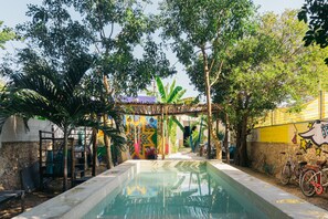 A swimming pool with a stone wall and a mural, surrounded by trees and a bicycle.