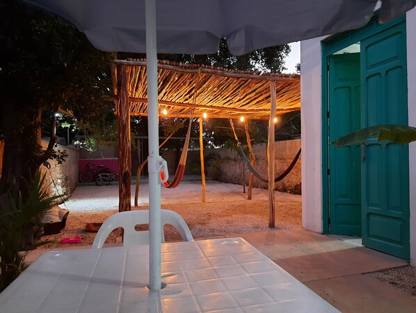 An outdoor patio with a white table, a hammock, and a covered seating area with string lights.
