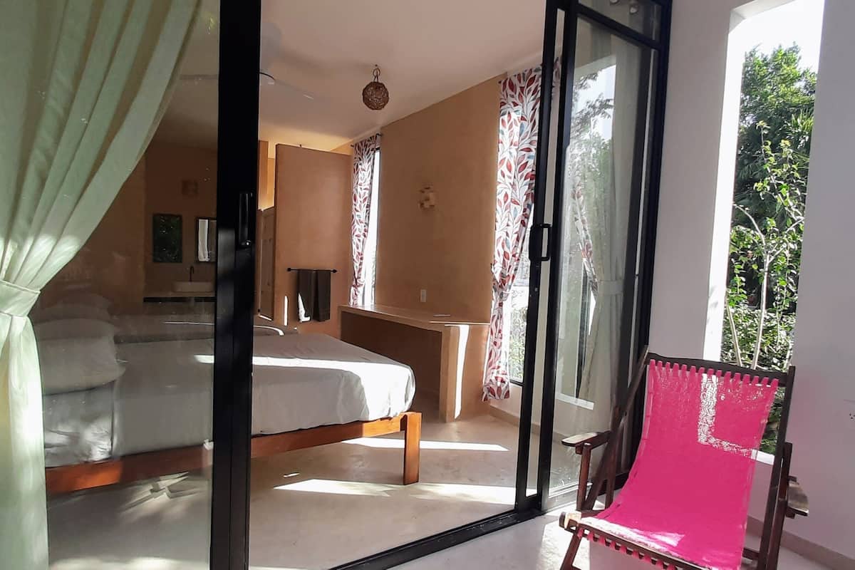 A bedroom with a bed, a desk, and a chair. There is a sliding glass door leading to a balcony.