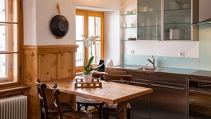 A modern kitchen with wooden cabinetry, a stainless steel refrigerator, and a dining area with a wooden table and chairs. - Chesa Chascharia 1 by Interhome (Samedan)