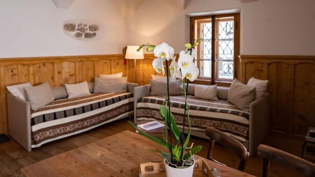A cozy room with a wooden ceiling, a sofa, a table, and a window with bars. - Chesa Chascharia 1 by Interhome (Samedan)