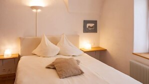 A bedroom with a bed, two bedside tables, a nightstand, a wall-mounted picture, and a radiator. - Chesa Chascharia 1 by Interhome (Samedan)