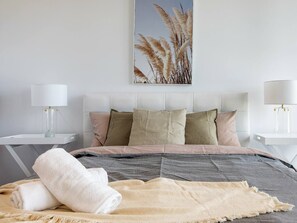 Ein modernes Schlafzimmer mit einem Bett, Kissen, einer Decke und zwei Nachttischen mit Lampen.