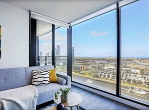 Ein modernes Wohnzimmer mit einem grauen Sofa, einem kleinen runden Tisch und einem großen Fenster mit Blick auf die Stadt.