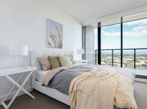 Ein modernes Schlafzimmer mit einem großen Bett, einem Nachttisch, einem Fenster mit Blick auf die Stadt und einem Wandbild.
