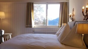 Une chambre d’hôtel avec un grand lit, une table de chevet avec une lampe, une chaise et une fenêtre avec des rideaux.