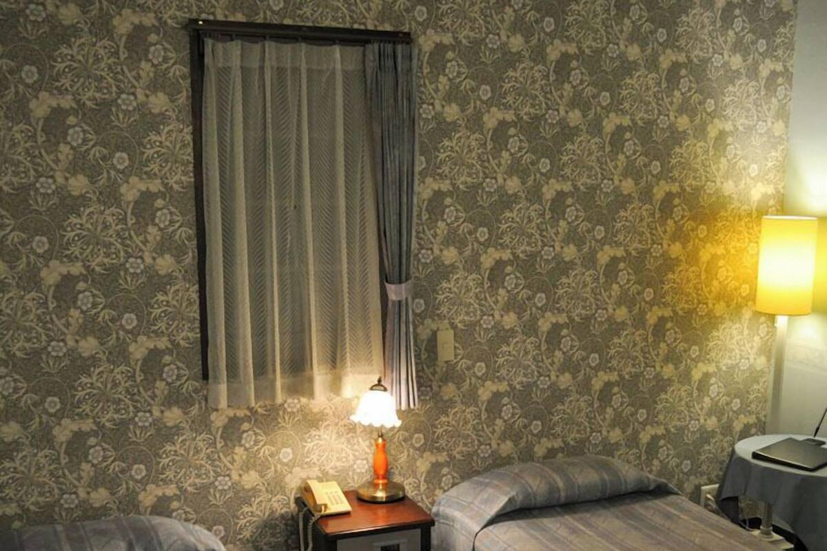 A room with two beds, a nightstand with a lamp, a telephone, and a table with a lamp.