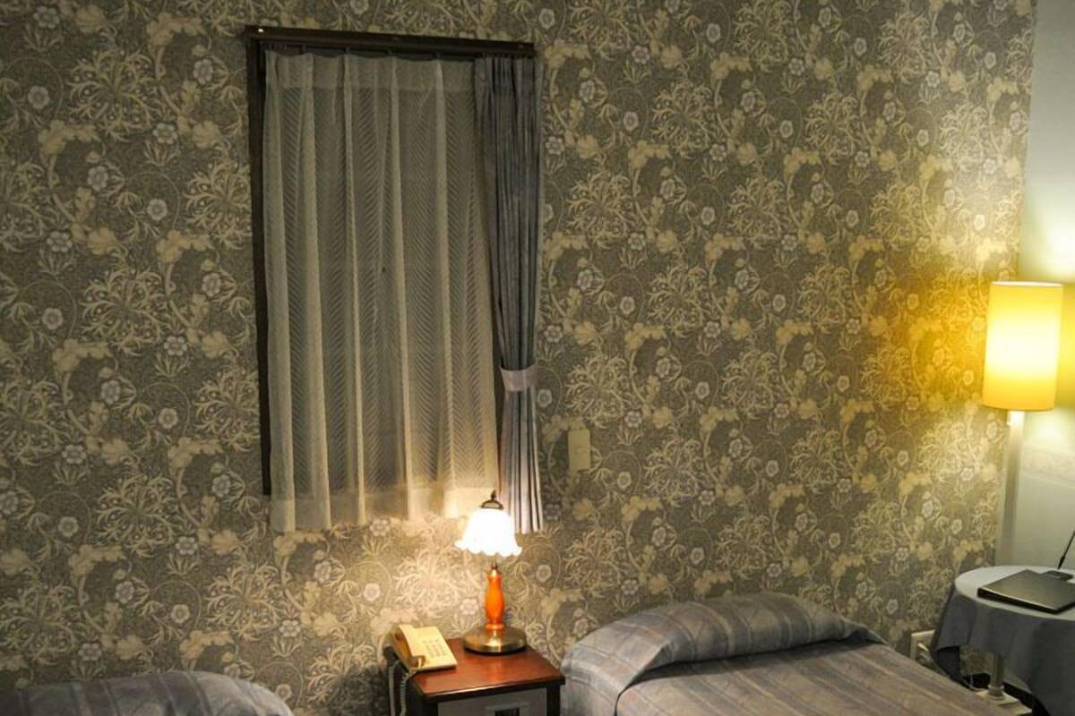 A room with two beds, a nightstand with a lamp, a telephone, and a small table with a lamp.