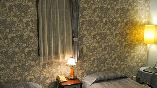 A room with two beds, a nightstand with a lamp, a telephone, and a small table with a lamp. - Camelia Inn Yukitsubaki (Kanazawa)