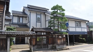 A traditional Japanese building with a tiled roof, a wooden gate, and a sign indicating a pedestrian crossing. - Camelia Inn Yukitsubaki (Kanazawa)